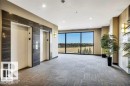Spacious common area featuring two elevators with wood-finish paneling, recessed lighting, and large windows showcasing distant trees and open space - 607 11080 Ellerslie Road, Edmonton, AB  - Indoor Photo Showing Other Room 