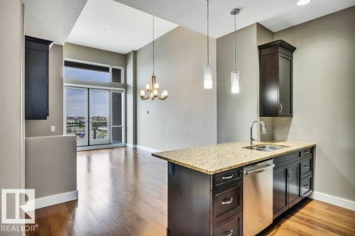 Kitchen island with a light-toned granite countertop, stainless steel sink, and dark wood cabinetry - 607 11080 Ellerslie Road, Edmonton, AB - Indoor Photo Showing Kitchen With Double Sink