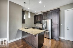 Kitchen featuring a granite-topped island with an undermount sink, dark wood-finish cabinetry, stainless steel appliances, and wood-finish flooring - 