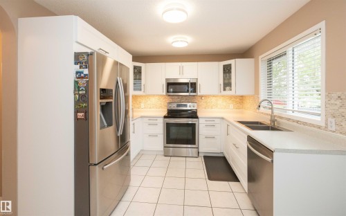 U-shaped kitchen featuring white cabinetry, stainless steel appliances, a mosaic tile backsplash, and light-toned countertops - 10739 109 Avenue, Westlock, AB 