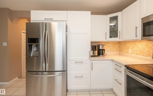 Contemporary kitchen featuring white cabinetry with brushed nickel hardware, stainless steel appliances, a mosaic tile backsplash, light-toned countertops, and tile flooring - 10739 109 Avenue, Westlock, AB 