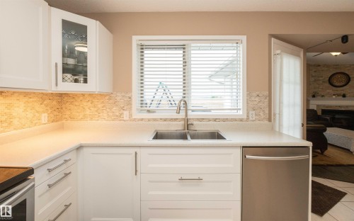 Kitchen featuring a double basin stainless steel sink, white cabinetry with brushed nickel hardware, light-toned countertop, mosaic tile backsplash, and a stainless steel dishwasher - 10739 109 Avenue, Westlock, AB 
