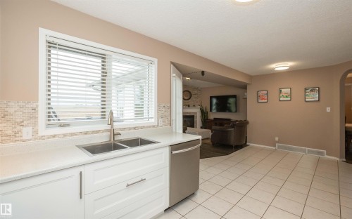 Kitchen featuring a dual-basin stainless steel sink, white cabinetry, integrated dishwasher, and mosaic tile backsplash - 10739 109 Avenue, Westlock, AB 