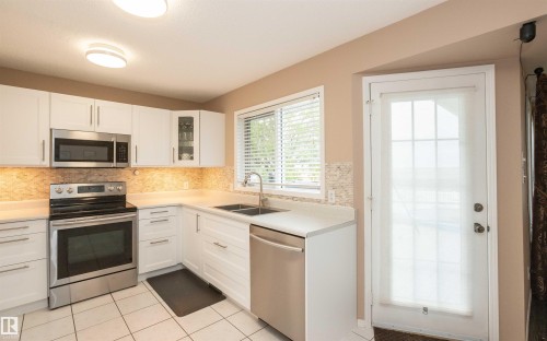 Modern kitchen featuring white cabinetry, stainless steel appliances, a light-toned countertop, and a tiled backsplash - 10739 109 Avenue, Westlock, AB 