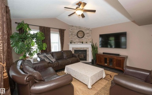 Living area featuring a vaulted ceiling with a ceiling fan, a fireplace with a stone-clad surround and white mantel, and wood-finish flooring - 10739 109 Avenue, Westlock, AB 