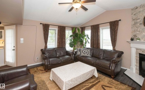 Living area featuring a vaulted ceiling with a ceiling fan, a stone-faced fireplace with a white mantel, and wood-finish flooring - 10739 109 Avenue, Westlock, AB 