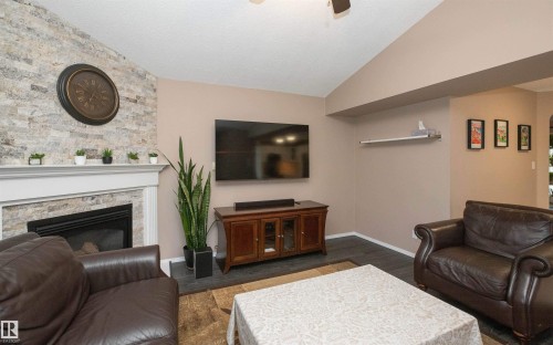 Living area featuring a floor-to-ceiling stacked stone fireplace with a white mantel, dark wood-finish flooring, and a vaulted ceiling - 10739 109 Avenue, Westlock, AB 