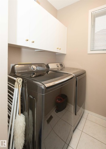Laundry area featuring white cabinetry with gold-tone hardware, a window with blinds, and tiled flooring - 10739 109 Avenue, Westlock, AB 