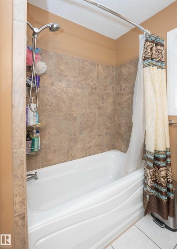 Bathtub and shower combination featuring neutral-toned wall tiles with a decorative accent band, a white tub, and a curved shower rod - 10739 109 Avenue, Westlock, AB 
