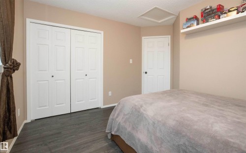 Room featuring wood-finish flooring, two sets of white bi-fold closet doors, and a neutral wall color - 10739 109 Avenue, Westlock, AB 