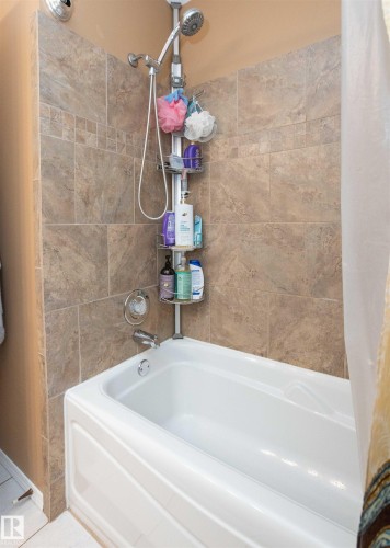 White bathtub with a chrome faucet and shower head, featuring full-height stone-look tile surround with a decorative band - 10739 109 Avenue, Westlock, AB 