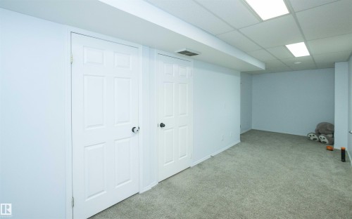 Finished basement space featuring light gray carpeting, neutral wall color, two panel doors, and a drop ceiling with recessed lighting - 10739 109 Avenue, Westlock, AB 