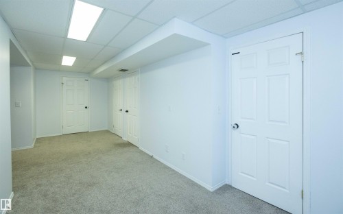 Carpeted room featuring white walls, a drop ceiling with integrated lighting, and multiple panel doors - 10739 109 Avenue, Westlock, AB 