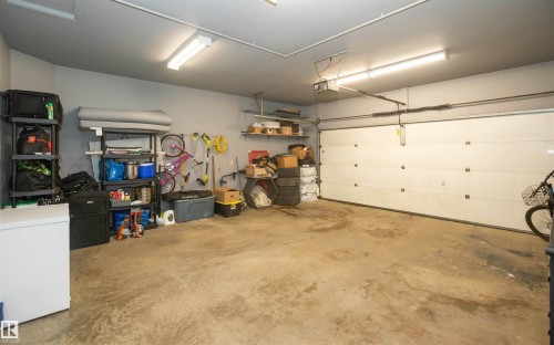 Spacious garage featuring a large overhead door, concrete flooring, and ample wall shelving for storage - 10739 109 Avenue, Westlock, AB 