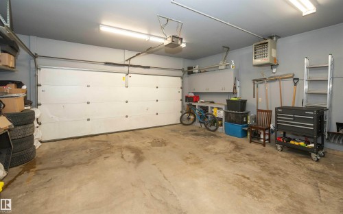 Spacious garage featuring a large automatic overhead door, concrete flooring, overhead fluorescent lighting, wall-mounted cabinetry, and a built-in wall heater - 10739 109 Avenue, Westlock, AB 