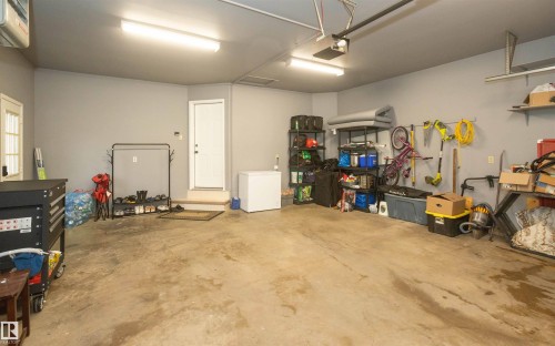 Spacious garage with light gray walls, concrete flooring, dual fluorescent overhead lighting, and built-in shelving - 10739 109 Avenue, Westlock, AB 