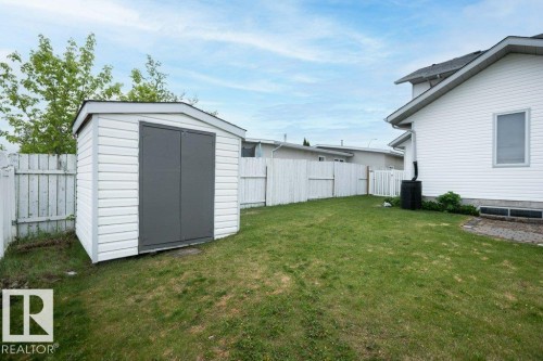 Spacious backyard featuring a white vinyl-sided storage shed with dark gray doors, a white wooden fence, and a green lawn - 10739 109 Avenue, Westlock, AB 