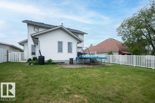 Expansive backyard featuring a manicured lawn, a concrete patio, and a white picket fence - 10739 109 Avenue, Westlock, AB 