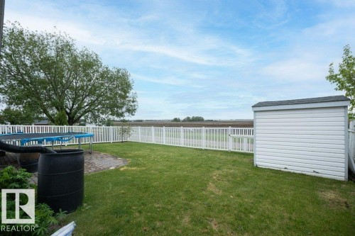 Expansive backyard featuring a manicured lawn, a white vinyl privacy fence, and a storage shed with horizontal siding - 10739 109 Avenue, Westlock, AB 