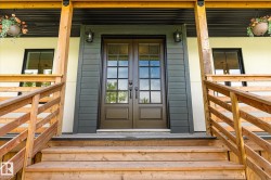 Entryway featuring double doors with glass panes, wood steps, coordinating wood railings, black exterior sconces, and dark horizontal siding accents - 