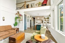Two-story living area with wood-finish flooring, a stone-accented kitchen, and an upper-level balcony with metal balusters - 