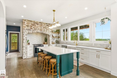 Gourmet kitchen featuring a stone-clad range hood, large center island with seating, extensive white cabinetry, gold-finish fixtures, and wood-finish flooring - 59102 Rge Road 234, Rural Westlock County, AB 