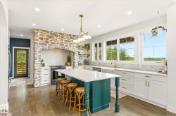 Gourmet kitchen featuring a stone-clad range hood, large center island with seating, extensive white cabinetry, gold-finish fixtures, and wood-finish flooring - 