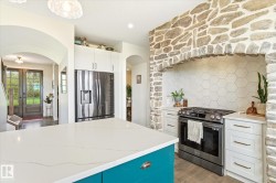 Gourmet kitchen featuring a stone archway, hexagonal tile backsplash, stainless steel range, and a spacious island with a white countertop - 