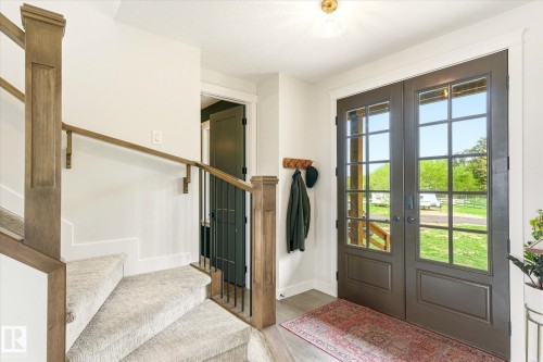 Entryway featuring double glass-paneled doors, wood-finish flooring, a contemporary ceiling light fixture, and a carpeted staircase with wood-finish newel posts and handrails - 59102 Rge Road 234, Rural Westlock County, AB 