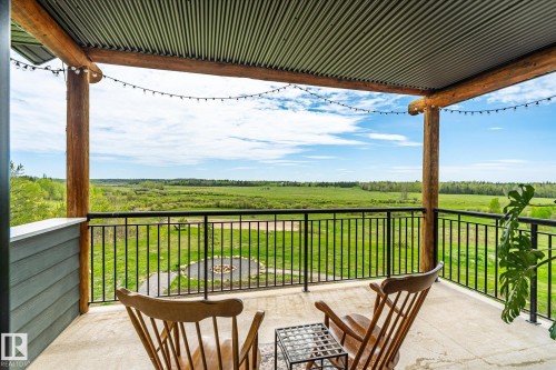 Covered outdoor deck with exposed log beams, corrugated metal ceiling, dark metal railing, and concrete flooring - 59102 Rge Road 234, Rural Westlock County, AB 