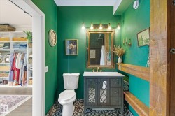 Bathroom featuring a dark green accent wall, patterned floor tiles, a vanity with a white countertop, and an ornate mirror with brass-finish lighting - 