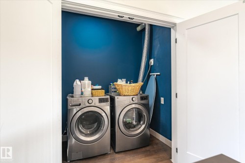 Dedicated laundry closet featuring a rich blue accent wall, modern front-loading washer and dryer, wood-finish flooring, and bright white trim - 59102 Rge Road 234, Rural Westlock County, AB 