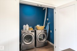 Dedicated laundry closet featuring a rich blue accent wall, modern front-loading washer and dryer, wood-finish flooring, and bright white trim - 