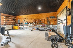 Spacious workshop featuring a concrete floor, wood-paneled walls, a dark corrugated metal ceiling, and built-in shelving units - 