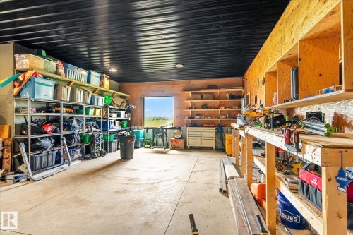 Spacious garage/workshop area featuring a corrugated metal ceiling, concrete flooring, built-in wooden shelving, and a large window - 59102 Rge Road 234, Rural Westlock County, AB 