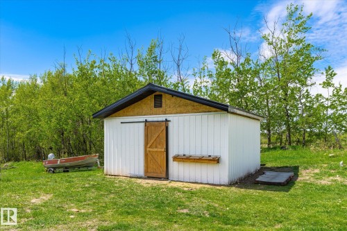 White storage building featuring a dark shingled roof, a natural wood-finish gable, and a wood-finish barn door on a black sliding track - 59102 Rge Road 234, Rural Westlock County, AB 