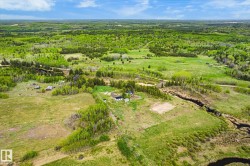 Expansive land parcel featuring a winding creek, varied tree coverage, open fields, and multiple structures - 