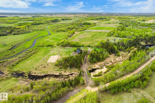 Expansive rural landscape featuring a winding waterway, a dirt road, dense green foliage, open fields, and a distant residence with outbuildings - 59102 Rge Road 234, Rural Westlock County, AB 