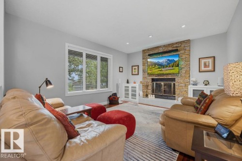 Living room featuring a stacked stone wood burning fireplace with an integrated media niche, hardwood flooring, and a large window with white louvered blinds - 31 Wentworth Crescent, St. Albert, AB - Indoor Photo Showing Living Room With Fireplace