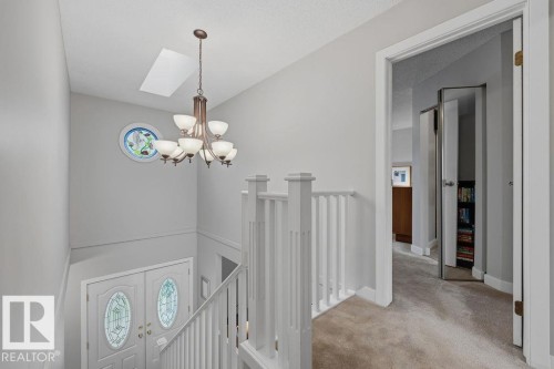 The upper level landing is open to below showing the modern staircase with white banister, newer skylight, overhead chandelier, and oval glass accented door - 31 Wentworth Crescent, St. Albert, AB - Indoor Photo Showing Other Room