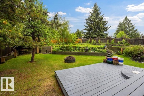 Expansive backyard featuring a multi-level garden, mature trees, a dedicated fire pit area, and a grey composite deck with a built-in circular step - 31 Wentworth Crescent, St. Albert, AB - Outdoor With Deck Patio Veranda With Backyard