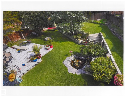 Expansive backyard featuring a multi-level deck, a rock-edged water feature, terraced landscaping with retaining walls, established trees, and lush green lawn. Photo taken in prior years when yard is in full bloom. - 31 Wentworth Crescent, St. Albert, AB - Outdoor