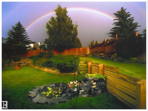 Lush tiered backyard featuring a natural stone pond, wood retaining walls, and mature trees. Photo taken in prior years when yard is in full bloom. - 31 Wentworth Crescent, St. Albert, AB - Outdoor With Backyard