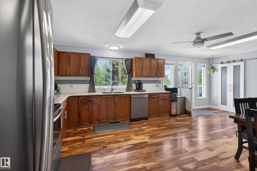 Spacious kitchen featuring wood-finish flooring, wood cabinetry, a light-toned countertop, and stainless steel appliances - 110 52308 Rr 214, Rural Strathcona County, AB 