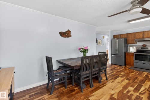 Open-concept dining area featuring wood-finish flooring, a contemporary ceiling fan, kitchen with wood cabinetry, and stainless steel appliances - 110 52308 Rr 214, Rural Strathcona County, AB 
