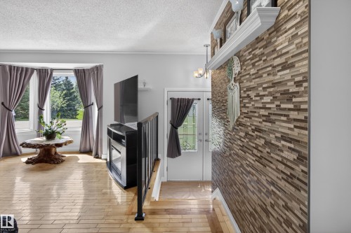 Hardwood-style flooring throughout, featuring a bay window with natural light, a built-in electric fireplace, and an accent wall with stacked stone-look tile - 110 52308 Rr 214, Rural Strathcona County, AB 