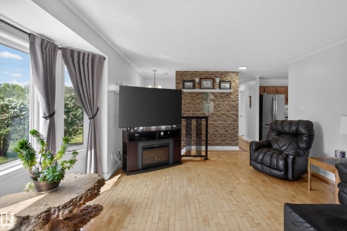 Spacious living area featuring light wood-finish flooring, a contemporary accent wall with stacked stone-look tile, and a large bay window - 110 52308 Rr 214, Rural Strathcona County, AB 