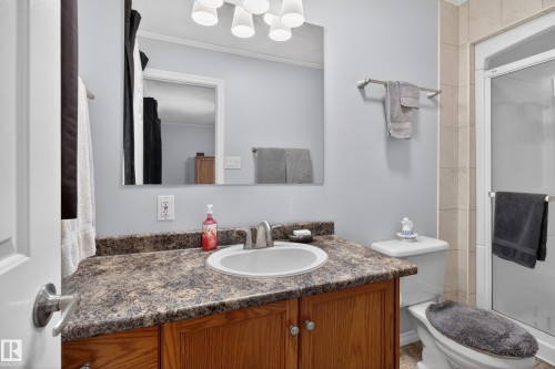 Bathroom featuring a wood-finish vanity with a speckled countertop and an integrated sink, polished chrome faucet, an enclosed shower with glass doors, and light-toned wall tiling - 110 52308 Rr 214, Rural Strathcona County, AB 