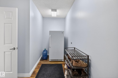 Hallway featuring wood-finish flooring, light blue walls, and a white paneled interior door with brushed nickel hardware - 110 52308 Rr 214, Rural Strathcona County, AB 