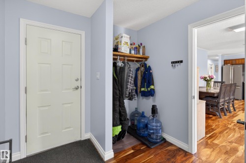 Entryway featuring a paneled door with brushed nickel hardware, coat closet with wood shelving, and wood-finish flooring - 110 52308 Rr 214, Rural Strathcona County, AB 